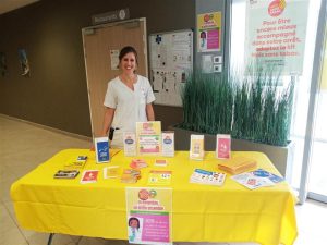 une femme infirmiere souriante devant une table jaune et des papiers dessus