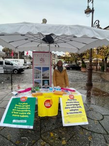 une femme souriante devant une table au marche avec de grandes affiches dessus
