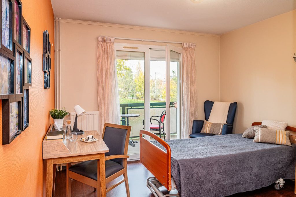 Chambre avec lit simple médicalisé, espace bureau et balcon avec vue le jardin